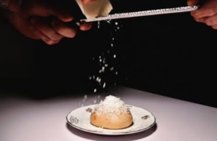 Euforia Bar Milan: Hands grating cheese over a bun on a plate. A culinary experience for gay men traveling in Milan, Italy.