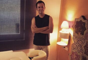Eugenio, gay massage therapist in Barcelona, stands confidently by a massage table. Travel advice for gay men seeking wellness services.