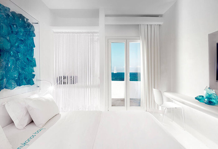 Mykonos Bay Resort & Villas room with ocean view. Beachfront gay hotel in Mykonos with pool. White interior, blue accents. Gay travel.
