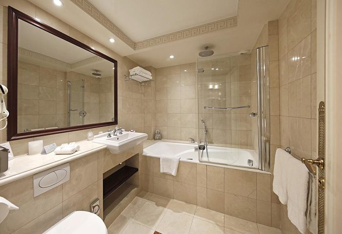 Hotel Napoleon Paris bathroom. Beige tile, tub/shower combo with glass screen, sink, toilet, large mirror. Near gay bars and saunas.