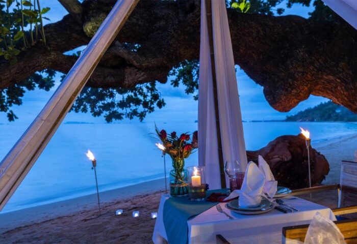 Romantic beach dinner at Explora Koh Phangan, a gay-friendly adults-only resort. Tiki torches and candles light up the idyllic setting.