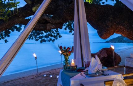 Romantic beach dinner at Explora Koh Phangan, a gay-friendly adults-only resort. Tiki torches and candles light up the idyllic setting.