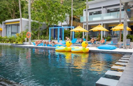 Explorar Koh Phangan adults-only resort pool scene. Gay-friendly beach hotel with men relaxing, yellow umbrellas, and duck floats.