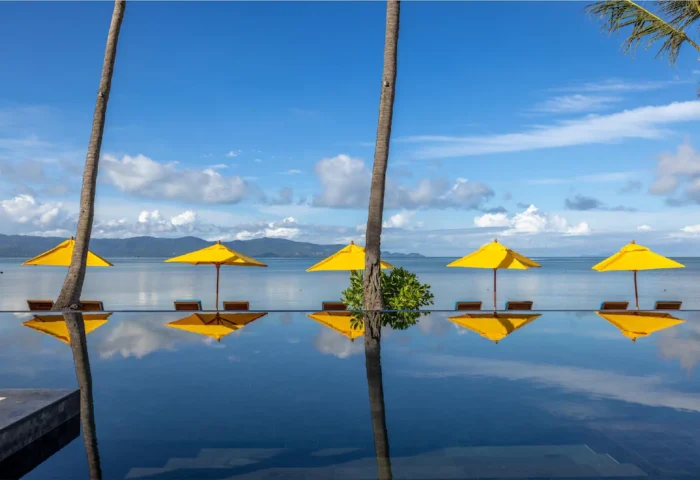 Infinity pool at Explora Koh Phangan, adults-only resort & spa. Yellow umbrellas & lounge chairs reflect in the water. Gay-friendly hotel.