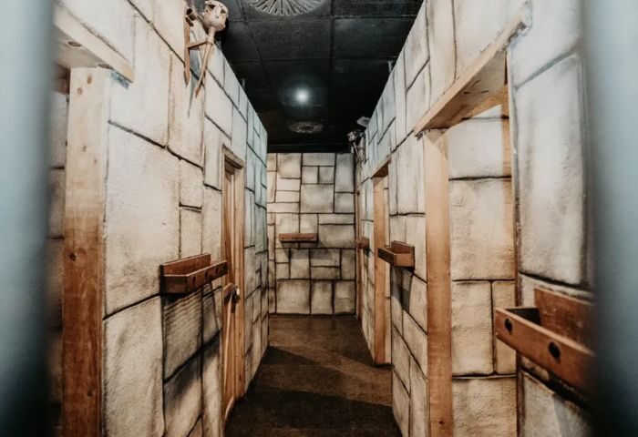 Hallway with stone walls, doors, and wooden shelves. A skull decoration is visible. Exxxtreme Cruising Club Gay Cruise Club.