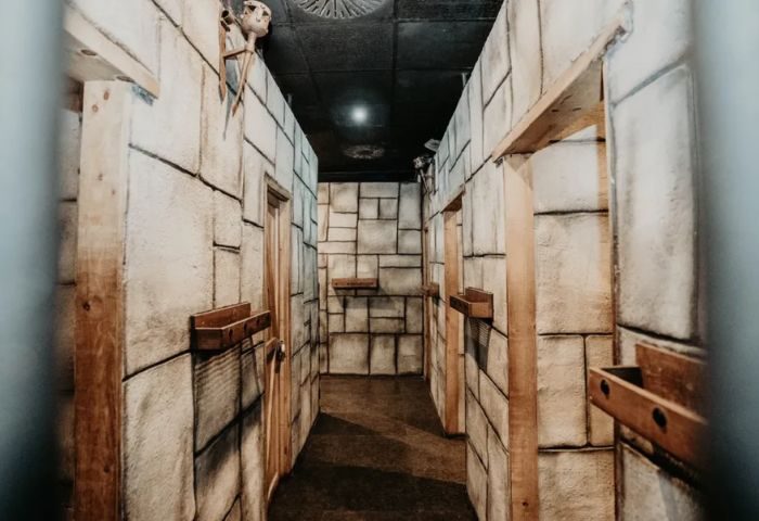 Hallway with stone walls, doors, and wooden shelves. A skull decoration is visible. Exxxtreme Cruising Club Gay Cruise Club.