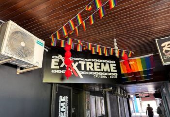 Entrance to Exxxtreme Cruising Club, a gay cruise club. Rainbow flags decorate the ceiling. Gay travel advice.