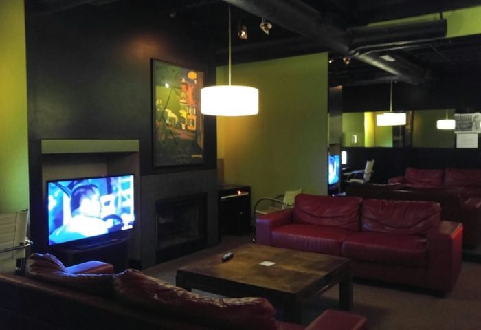 Vancouver's F212° Steam Gym lounge area. Red leather couches, TV, fireplace, and modern lighting create a relaxing space for gay men's travel.
