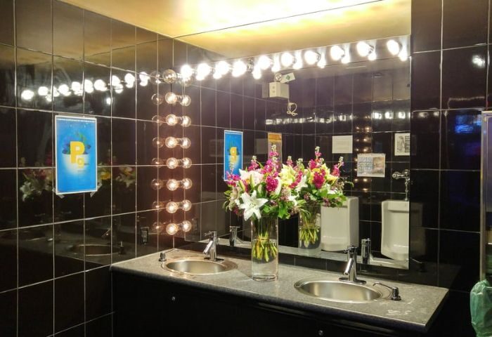 Steamworks Gym Vancouver bathroom. Black tile, bright lights, flowers, sinks, & urinal. Gay travel advice for a unique gym experience.