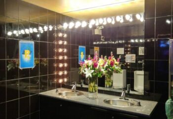 Steamworks Gym Vancouver bathroom. Black tile, bright lights, flowers, sinks, & urinal. Gay travel advice for a unique gym experience.