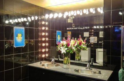 Steamworks Gym Vancouver bathroom. Black tile, bright lights, flowers, sinks, & urinal. Gay travel advice for a unique gym experience.