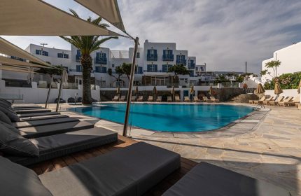 Poseidon Hotel Suites pool in Mykonos Town. Upscale gay hotel with sunbeds, palm tree, and blue accents. Last minute travel deals.