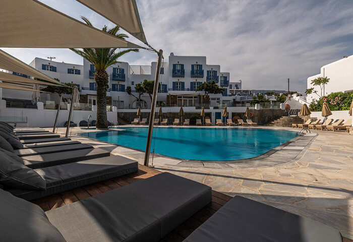 Poseidon Hotel Suites pool in Mykonos Town. Upscale gay hotel with sunbeds, palm tree, and blue accents. Last minute travel deals.