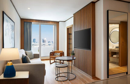 Sheraton Tel Aviv Hotel room for 3 people near Hilton Gay Beach. Luxury suite interior with TV, couch, and city view. Gay travel.