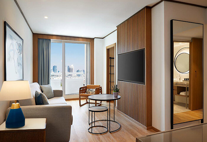 Sheraton Tel Aviv Hotel room for 3 people near Hilton Gay Beach. Luxury suite interior with TV, couch, and city view. Gay travel.