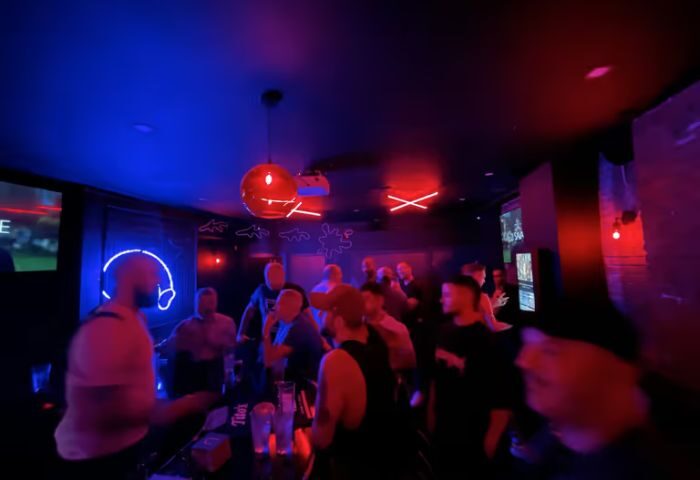 FLEX Gay Bar in New York. Interior view of a crowded gay bar with red and blue lighting, neon signs, and patrons socializing.