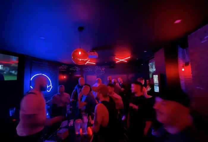 FLEX Gay Bar in New York. Interior view of a crowded gay bar with red and blue lighting, neon signs, and patrons socializing.