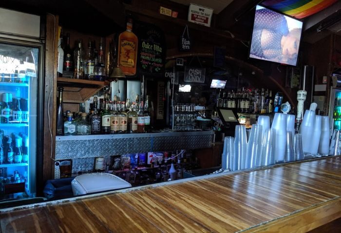 Falcon Long Beach bar interior. Bottles line the back bar, a rainbow flag hangs above a TV. Gay travel advice.