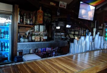 Falcon Long Beach bar interior. Bottles line the back bar, a rainbow flag hangs above a TV. Gay travel advice.
