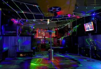 Falcon North's outdoor dancefloor. Gay bar with colorful lights, dance floor, and a plane wing overhead. Gay travel destination.