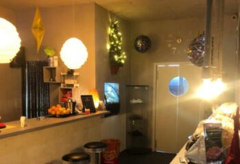 Fenix Sauna Milano interior. Bar area with stools, counter with fruit, and decorative lighting. Gay sauna travel advice.