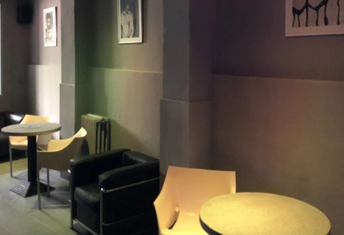 Lounge area at Fenix Sauna Milano. Tables, chairs, and artwork create a relaxed atmosphere for gay men's travel and sauna experience.