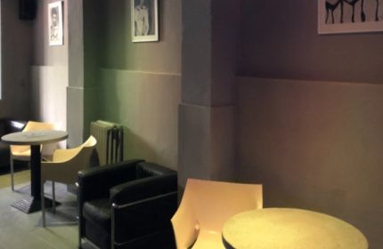 Lounge area at Fenix Sauna Milano. Tables, chairs, and artwork create a relaxed atmosphere for gay men's travel and sauna experience.