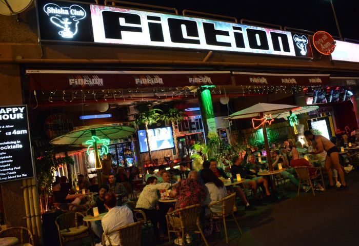 Fiction Bar, a gay bar in Gran Canaria, is bustling with patrons at night. The outdoor seating area is lively and inviting.
