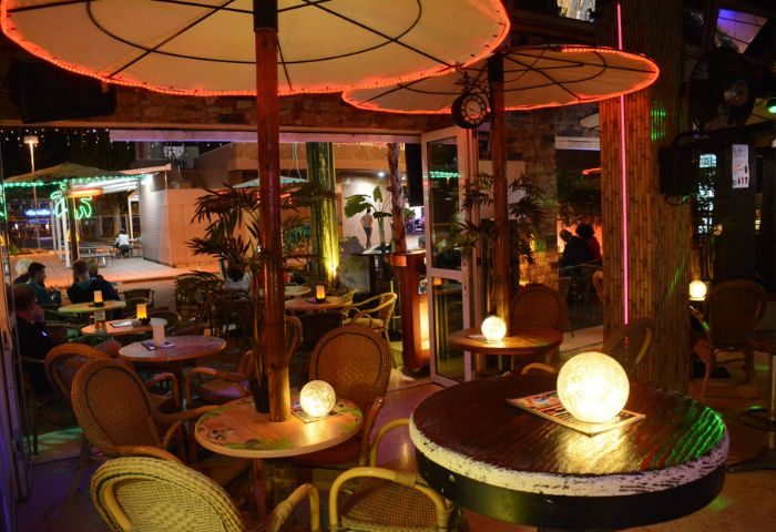 Fiction Gay Bar in Gran Canaria. Outdoor seating area with tables, chairs, and umbrellas. Warm lighting creates a welcoming atmosphere.