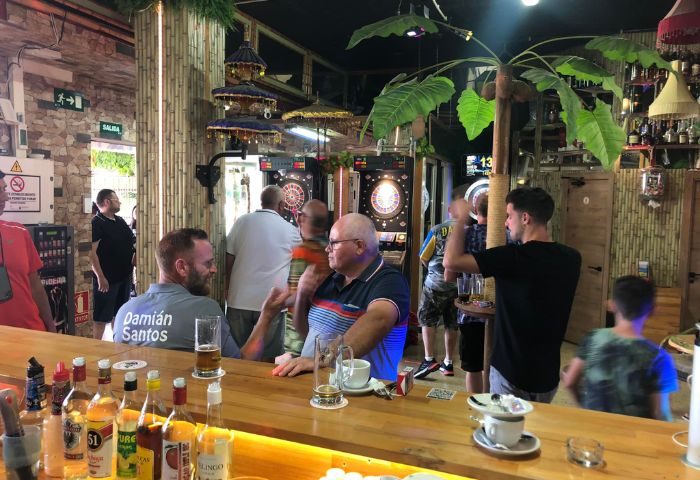 Fiction Bar, a gay bar in Gran Canaria. Patrons at the bar, some playing darts. A fun gay travel destination.