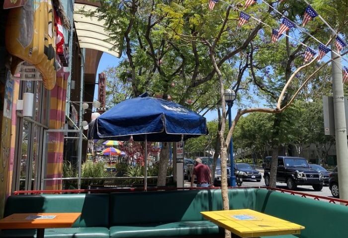 Outdoor seating at Fiesta Cantina, a gay bar in West Hollywood. Blue umbrellas shade green booths. American flags hang above the street.