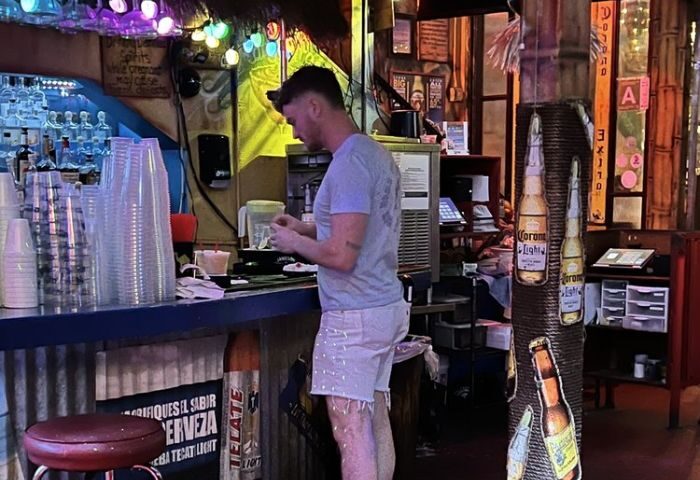 Fiesta Cantina service. Gay man at bar in Puerto Vallarta, Mexico. The cantina has a fun, festive atmosphere with Corona Light decor.