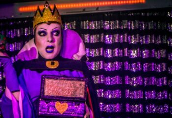 Drag queen at Finalmente Club, Lisbon. Person in Evil Queen costume with crown, cape, and heart-shaped box. Gay nightlife travel.