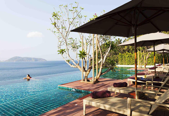U Zenmaya Phuket Resort rooftop pool view. Gay hotel in Phuket. Woman swimming, lounge chairs, umbrellas, and ocean view. Find cheap price.