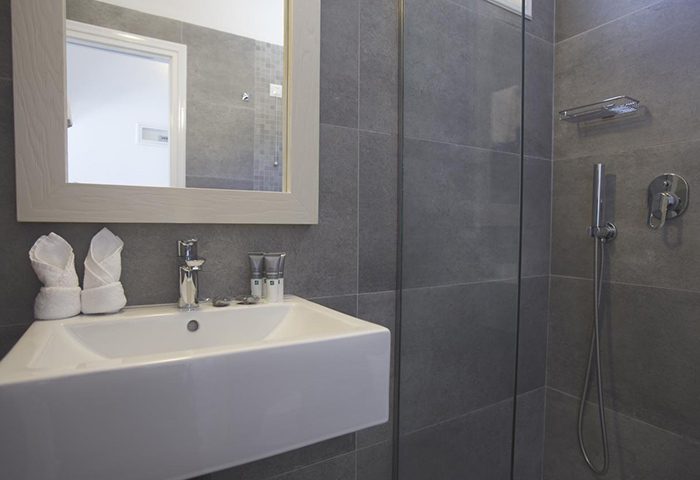 Marisso Hotel gay-friendly room for 3 in Mykonos Town: Modern bathroom with sink, shower, mirror, and gray tiles. Ideal gayborhood stay.