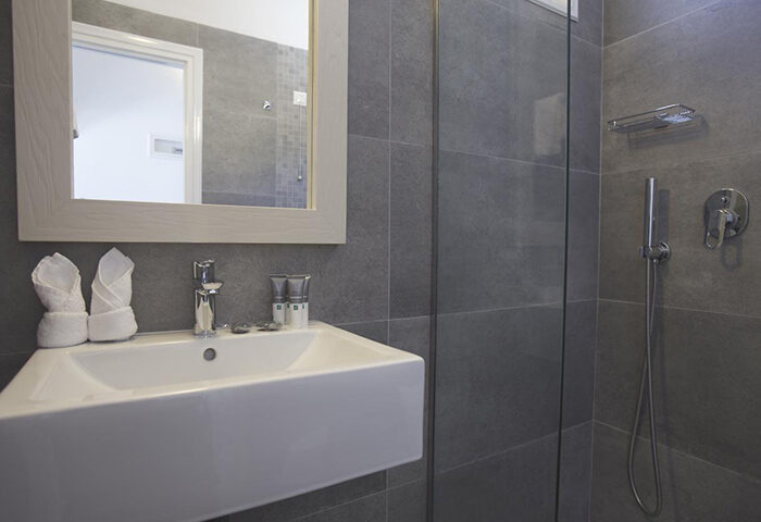 Marisso Hotel gay-friendly room for 3 in Mykonos Town: Modern bathroom with sink, shower, mirror, and gray tiles. Ideal gayborhood stay.