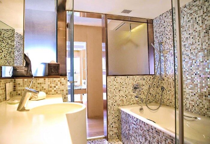 Bathroom in Hong Kong hotel near gay bars. Mosaic tile decor, modern sink, bathtub, and glass shower. Find cheap hotel on waterfront.