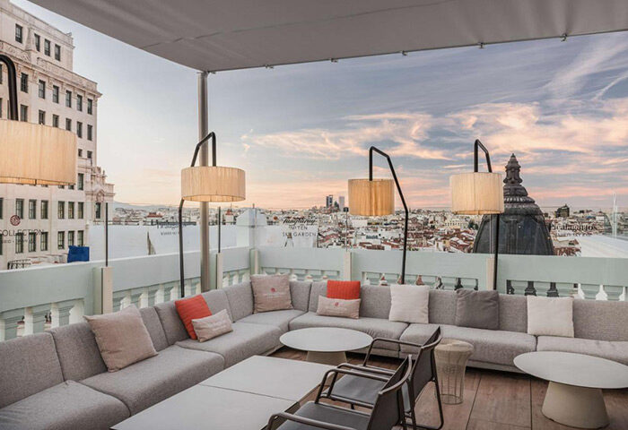 Rooftop lounge at NH Collection Madrid Gran Via, a cheap gay-friendly hotel in Madrid's gayborhood. City view, seating area, lamps.