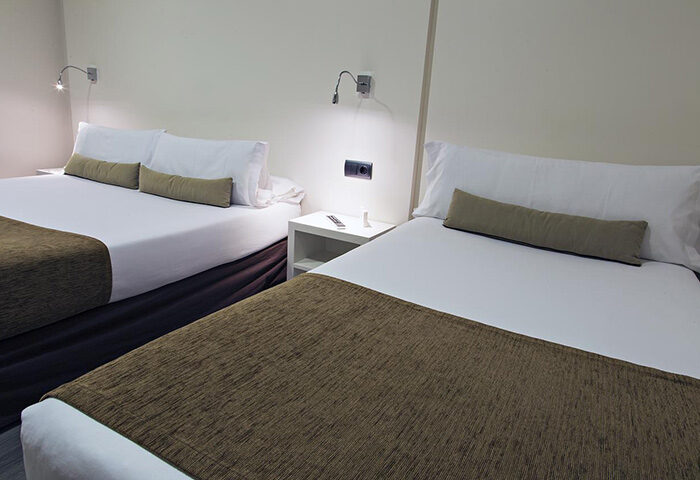BCN Urbaness Hotels Del Comte room for 3 persons. Find cheap price gay hotel room in Barcelona. Two beds with white sheets and brown throws.