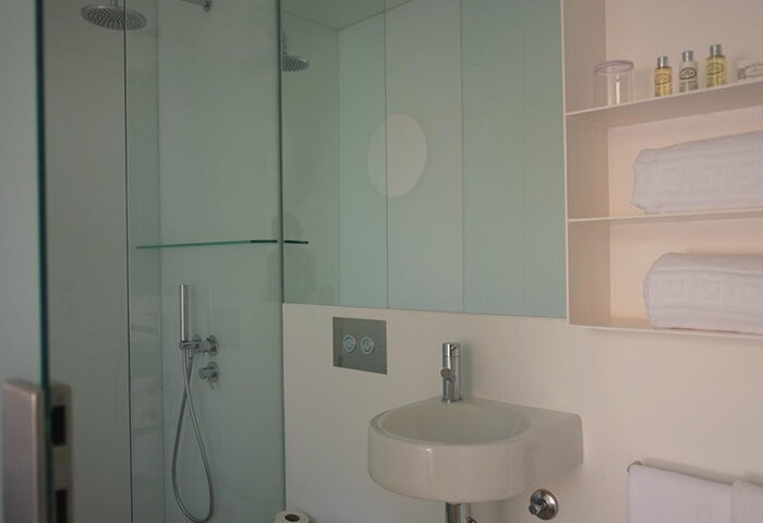 Bathroom at The Late Birds Lisbon, a gay urban resort. Modern design with shower, sink, and shelves. Gay men's hotel in Lisbon.