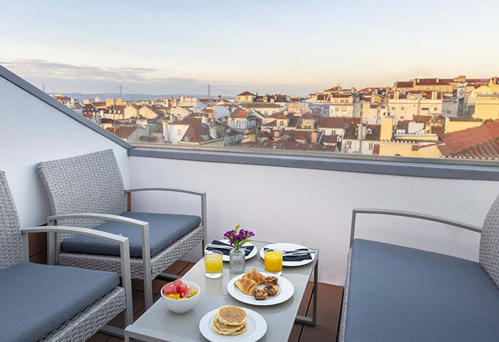 9Hotel Mercy Lisbon upscale gay hotel balcony view. Breakfast with pancakes, fruit, juice. Lisbon cityscape background.