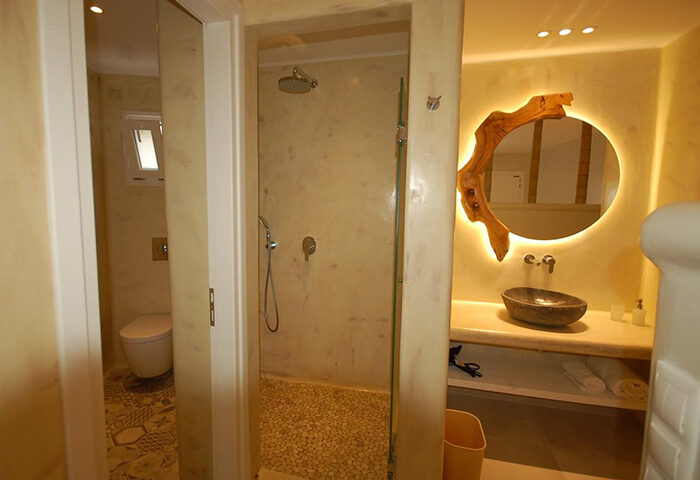 Sahas Suites Mykonos bathroom. Find cheap self-catering apartment near gay beaches with shower, sink, and unique wood-framed mirror.