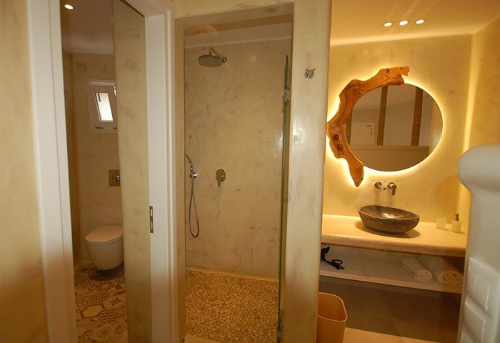 Sahas Suites Mykonos bathroom. Find cheap self-catering apartment near gay beaches with shower, sink, and unique wood-framed mirror.