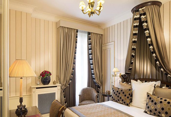 Hotel Napoleon Paris room with canopy bed. Gay hotel ideas in Paris gayborhood for gay men travelers. Luxury room decor with curtains, lamp, and chandelier.