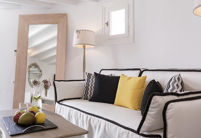 Absolute Mykonos Suites room for 4 people in Mykonos Town Gayborhood. Couch with pillows, fruit and drinks on table, mirror and lamp.
