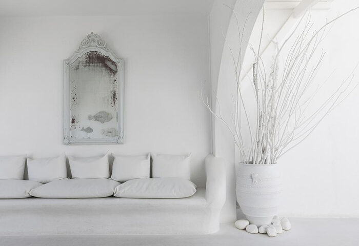 Mykonos Bay Resort & Villas room: All-white decor with sofa, pillows, mirror, and vase with branches. Find gay hotel in Mykonos Town.