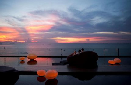 Hilton Pattaya beachfront luxury gay hotel. Couple relaxes poolside at sunset, enjoying last minute travel deals.