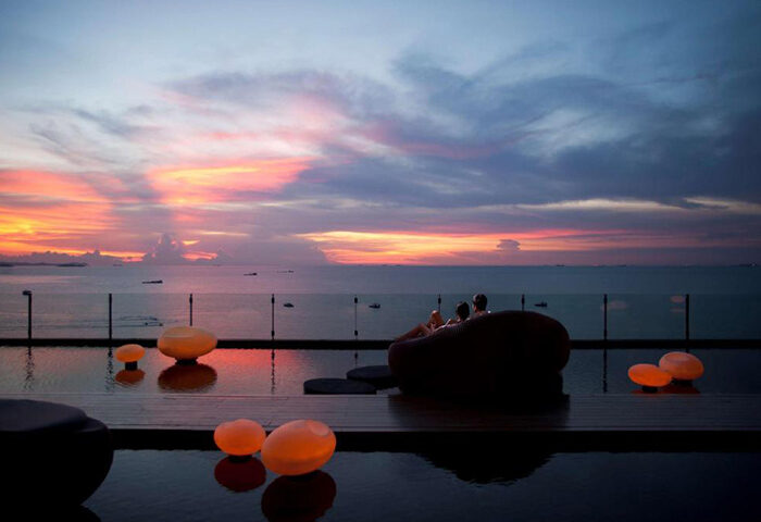 Hilton Pattaya beachfront luxury gay hotel. Couple relaxes poolside at sunset, enjoying last minute travel deals.