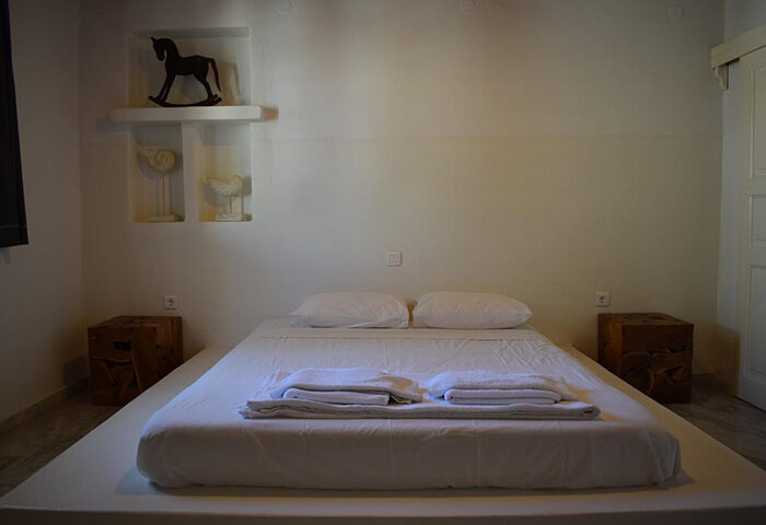 Mykonos Town gay hotel room. Minimalist design, white linens, wooden bedside tables. Find last minute cheap price for gay travel in Chora, Greece.