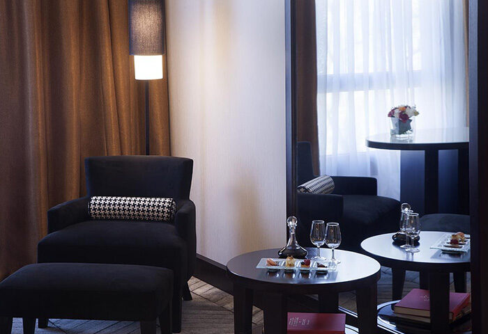 Sofitel Lisbon Liberdade luxury hotel room in Lisbon's gayborhood. Black armchair, ottoman, table with wine, and snacks. Elegant, modern design.